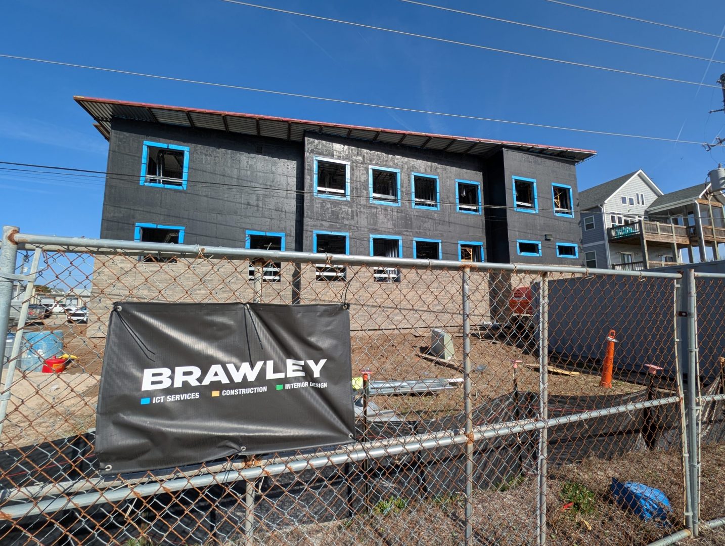 exterior side of a building under construction with a metal fence in front and a Brawley Company banner hanging
